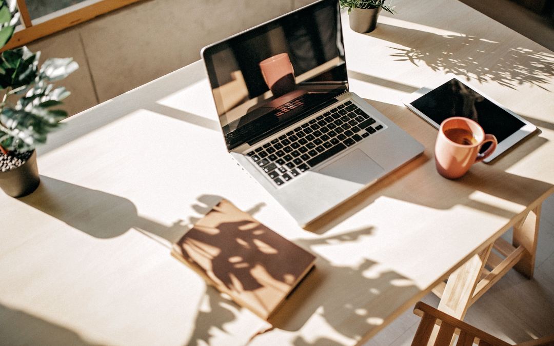 Bureau lumineux avec ordinateur, carnet et tasse de café pour illustrer une réflexion sur son business.
