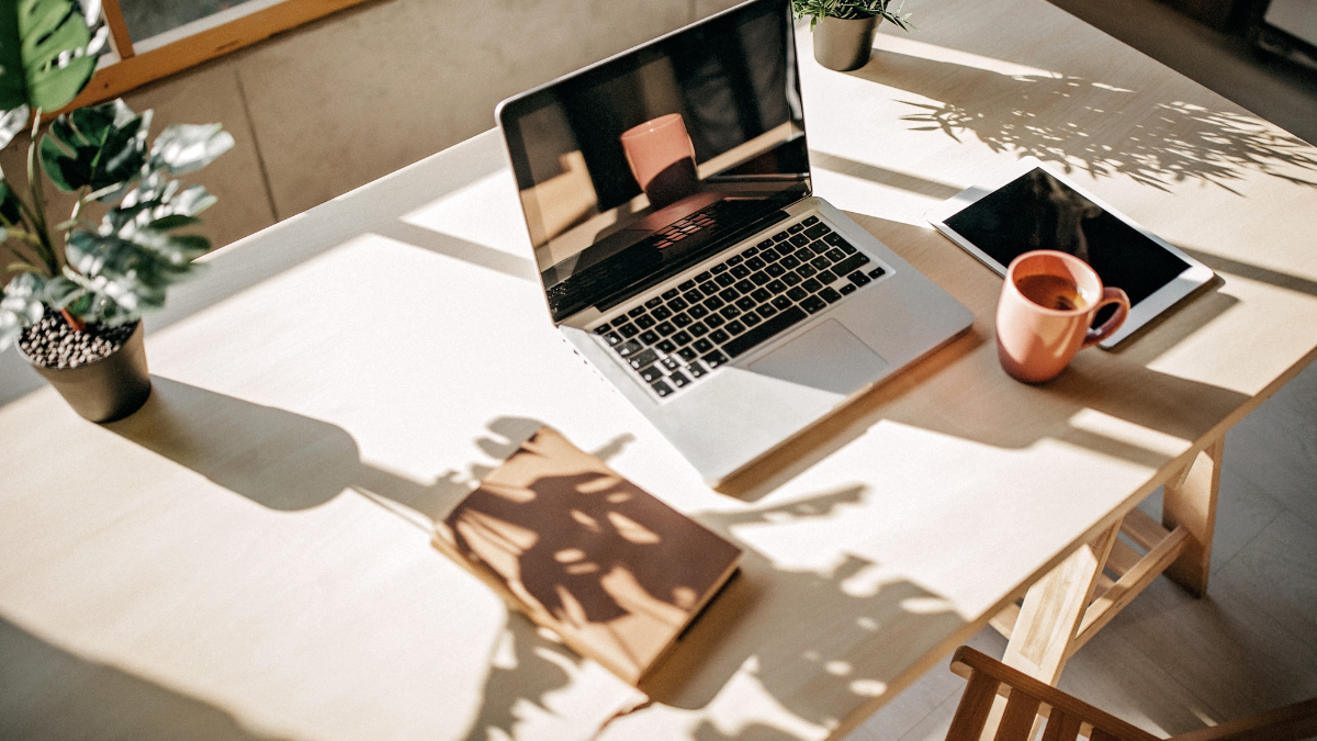 Bureau lumineux avec ordinateur, carnet et tasse de café pour illustrer une réflexion sur son business.